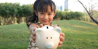 亚洲小孩抱着小猪储蓄罐迷人的微笑。