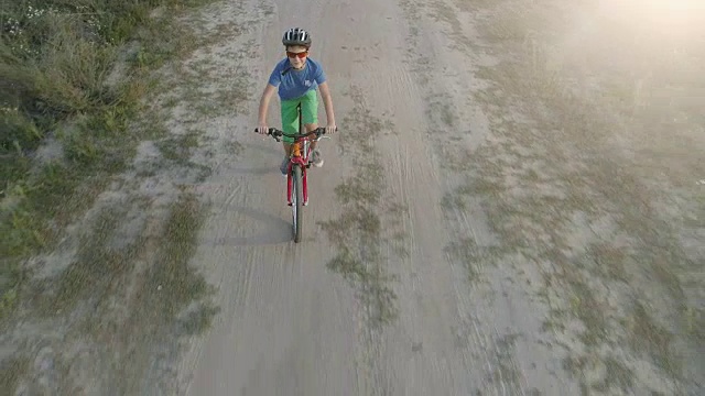 日落时分，男孩在乡间小路上骑自行车。鸟瞰图。4 k, UHD