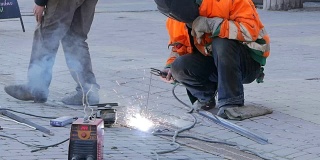 有面罩的人焊接金属零件。焊工正在街上工作。