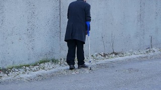 老年残疾人背景。这位老人拄着拐杖走在公共场合。视频素材模板下载