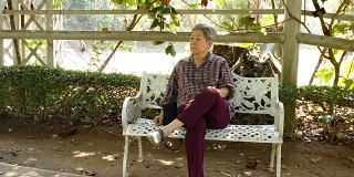 亚洲老妇人夏天坐在花园里。老年女性老年人在公园放松