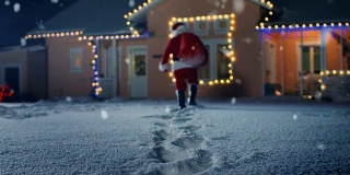 圣诞老人拿着红包，走进装饰着彩灯和花环的田园小屋的前院。圣诞老人在晚上带来礼物和礼物。神奇的新年夜与飘落的雪。