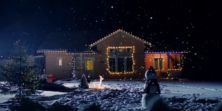 为平安夜装饰灯和花环的田园小屋。前院有圣诞树和雪人。轻柔的雪花在夜晚安详地飘落。