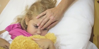 生病的小女孩在发烧。小孩发烧:女人抚摸小孩的头。特写镜头。