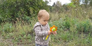 一个小男孩手里拿着一个玩具，正在公园外的秋日里迈出他的第一步。