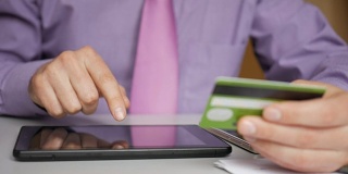 一位身穿紫色衬衫、打着领带的商人正在向网上银行付款。在数字平板电脑上用信用卡在线购物。