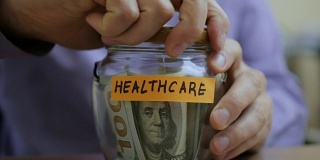 一个白人男人把一个玻璃罐子放在抽屉里，里面装着他未来的医疗储蓄