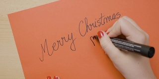 女孩用黑色记号笔在一张红纸卡片上写着圣诞快乐，准备送给她的男朋友