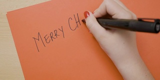 女人用黑色记号笔在红纸上用大写字母写着圣诞快乐