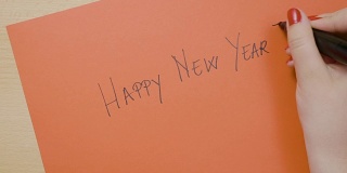 年轻女性用黑色记号笔在红纸上写下新年快乐