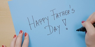女孩用红指甲在蓝色的纸上写父亲节快乐
