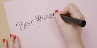 女性用黑色记号笔在粉红色的纸上用大写字母写下最美好的祝愿