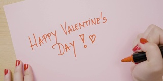 女人用红色记号笔在粉红色的纸上用大写字母写下“情人节快乐”