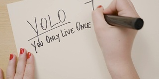 少女女性的手用红色指甲油写yolo你只活一次的励志格言在白纸上用黑色记号笔