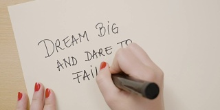 女性用黑色记号笔在白纸上写下梦想大、敢于失败的感叹号励志名言