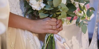 美丽的新娘捧花，年轻的新娘穿着白色婚纱。近距离的一大束新鲜的白玫瑰和郁金香花在女性的手中。匿名新娘手捧鲜花