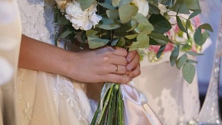 美丽的新娘捧花，年轻的新娘穿着白色婚纱。近距离的一大束新鲜的白玫瑰和郁金香花在女性的手中。匿名新娘手捧鲜花视频素材模板下载