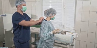 一队戴着口罩的医生正在为手术做准备。助手帮助外科医生穿上无菌的晨衣。医疗器械。健康理念，在医院工作。诊所设备