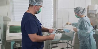 一名女外科医生从包裹中拿出一件无菌的晨衣。一队戴着口罩的医生正在为手术做准备。医疗器械。健康理念，在医院工作。诊所设备