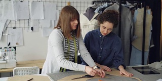 经验丰富的女裁缝正在教她的助手在织物上勾勒服装图案。年轻女子专注于过程，仔细观察并提出问题。