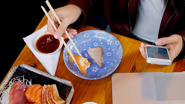 一个女人在4k餐厅边吃寿司边玩手机