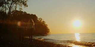 后视图-年轻夫妇沿着海滨散步在日落