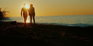 日落时分，在海边或湖边散步的情侣剪影。美丽的阳光。亚洲男人和白人女人