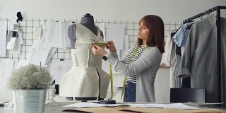 年轻迷人的女裁缝正在用胶带测量裁缝的假人，以便用这些尺寸做新衣服。忙碌的一天在服装车间的概念。