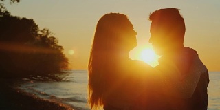 浪漫的多民族情侣在夕阳下拥抱，站在海边。互相看着对方