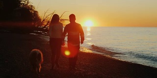 一对浪漫情侣的剪影。日落时分，在湖边或海边遛狗