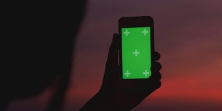 剪影女人的黄昏时分用智能手机的色度键拍摄城市景观