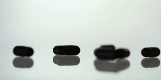药片散布在白色的背景上。黑色的药丸。缓慢的运动。片的背景