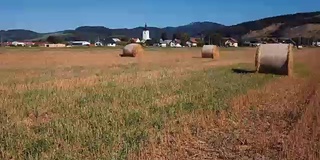 在有圆草堆的田野上空低空飞行。风景如画的小村庄和山峦为背景。