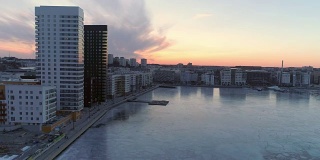 航拍现代公寓楼旁边的结冰的湖，瑞典斯德哥尔摩。日落时分，一架无人机飞过当代住宅区上空