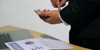 4K商务人员在会议桌上触摸手机团队工作，白皮书是计划汇总报告的文件，白皮书放在电脑笔记本上。