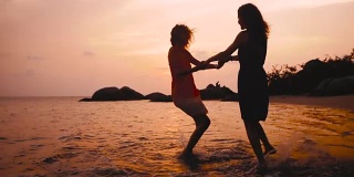 夕阳西下，两个快乐的女孩在沙滩上手拉手跳舞