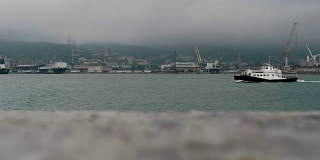 一艘巡逻艇驶过一个工业港口城市的海湾。