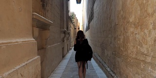 一个年轻女孩走在城市街道的老区的后视图