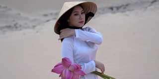 美丽的越南人捧着粉红莲花在白色沙丘沙漠上行走的4K电影，越南