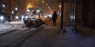 在冬天的大雪中，人们和汽车在夜晚沿着街道行驶