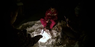 晚上一群人在雪地上点燃篝火，炸香肠