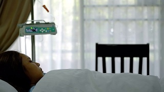 年轻的亚洲病人女人躺着，在医院VIP房间的床上睡着了模糊运动输液泵机和窗帘。视频素材模板下载