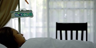 年轻的亚洲病人女人躺着，在医院VIP房间的床上睡着了模糊运动输液泵机和窗帘。