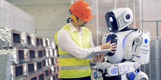 男性工人与机器人交谈，在平板电脑上向机器人显示信息，然后在机器人的显示器上输入信息。4 k。