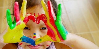 特写的亚洲女孩做一个心形手势与彩色绘画她的手，慢动作拍摄100帧/秒