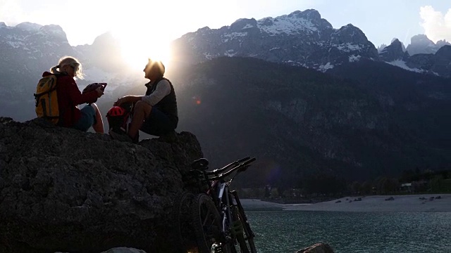 山地车夫妇在日出时在湖上的岩石上放松