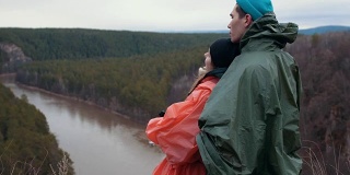 年轻的白种夫妇站在山坡上的山河享受美丽的自然