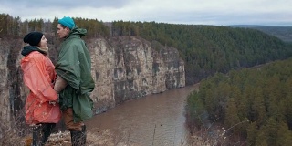 一对年轻的徒步旅行者站在悬崖边上，手拉手越过山河