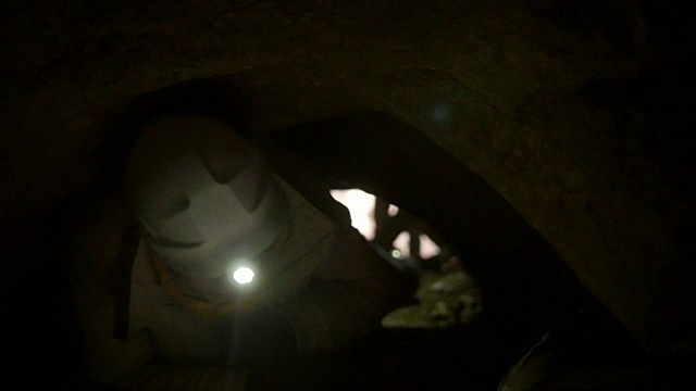 年轻的探险家们戴着头盔，手持手电筒，四肢着地在黑暗的洞穴中爬行