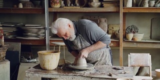 创造性的工匠正在工作与粘土在陶工的车轮创造小陶瓷碗。可见手工陶器、专业陶工设备和工具。